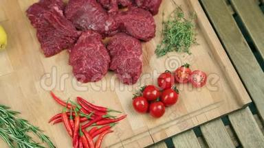 新鲜的肉做牛排在木板上。 炒肉，牛肉。 靠近西红柿，迷迭香，百里香，柠檬，红辣椒，蔓越莓..